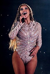 A woman holding a microphone, wearing a bodysuit
