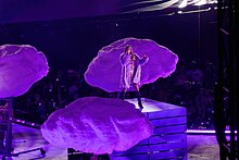 Taylor Swift performs on stage with three purple clouds around her