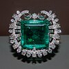 a square emerald set in a circular platinum brooch covered in diamonds