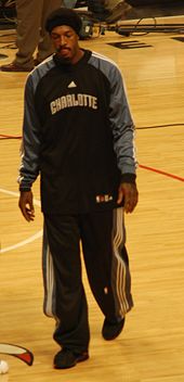 A man, wearing black pants and a black shirt with the word "CHARLOTTE" on the front, is walking on a basketball court.