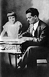 Photograph of Nestor Makhno writing at his desk, while his young daughter Elena climbs over the desk
