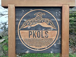 The photograph shows a carved wooden sign reading PKOLS with additional text on Mount Douglas, in Mount Douglas Park, in Saanich, British Columbia, Canada