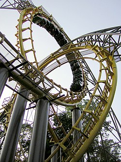 Pictured is the Loch Ness Monster roller coaster's interlocking loops from a ground-level view. A train is inverted in the top interlocking loop navigating from left to right on the bright yellow track.