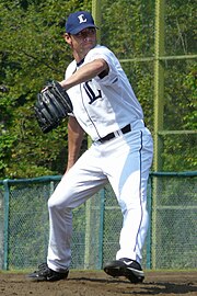 A man wearing a white baseball uniform with a navy blue "L" on the chest, a navy blue cap with a white "L" on the center, and a black glove on his left hand in the midst of pitching a ball