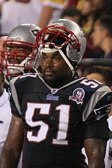 Jerod Mayo standing on the sideline in his patriots uniform and helmet, the helmet resting on his forehead.