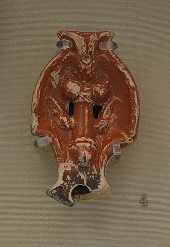 A terracotta lamp covered in a red slip glaze, with a phallus moulded on the top.