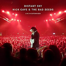 A man stands in the centre of a large arena illuminated by red light. He covers his face with a white towel. Several hundred people surround him from all sides. Uppercase white text at the top centre of the image reads "Distant Sky", "Nick Cave & the Bad Seeds" and "Live in Copenhagen" in three lines.