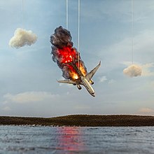A toy aeroplane on fire in the sky about to crash into the ground, with the plane, fire and surrounding clouds held by strings