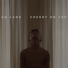 A young boy without a shirt is facing upwards towards the title of the song.