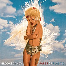 A blond topless woman stands over an image of a blue sky. She is wearing a large chastity belt, and the words feature the name of the song and the singer's name.