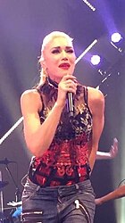 The singer appears in a red outfit and jeans while performing the song live.