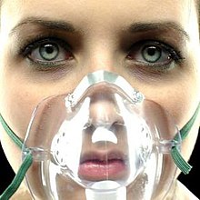 A woman facing forward with a breathing mask covering her mouth and nose