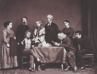 Stage photograph showing group of 3 women and five men in everyday Victorian clothes