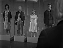 Copies of Barbara, the Doctor, Vicki, and Ian stand upright, emotionless, inside glass boxes. The Doctor's shoulder can be seen overlooking them.