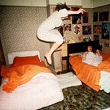 A photo of someone jumping off a bed while someone else is lying in an adjacent bed