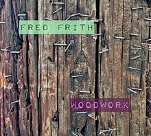 A colour photograph of wooden slats that fill the entire image; the slats are held together by metal staples; the letters "Fred Frith" in green appear at the top left of the picture, and "Woodwork" in pink at the bottom right