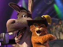 A screenshot from Shrek 2, depicting the characters Donkey and Puss in Boots, in front of a microphone